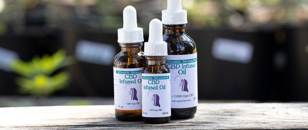 Three amber dropper bottles of Double Strength CBD Infused Oil in 250mg, 500mg, and 1000mg sizes on a wooden surface.
