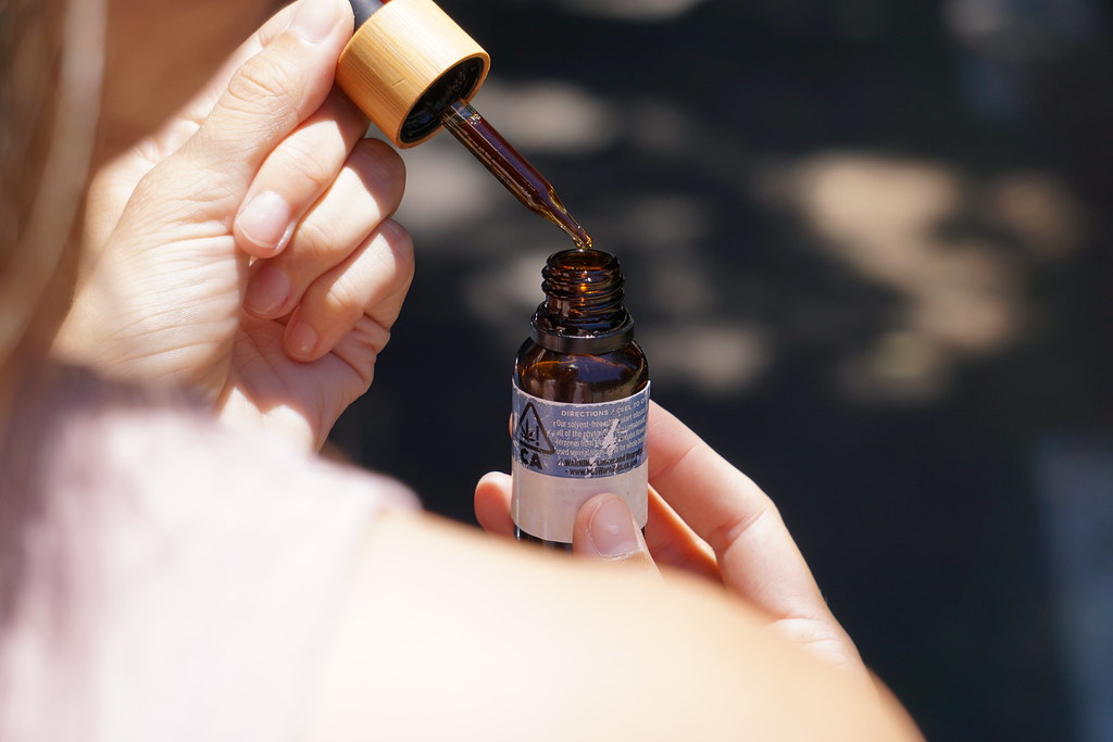 Hand holding a dropper over a small amber tincture bottle in sunlight